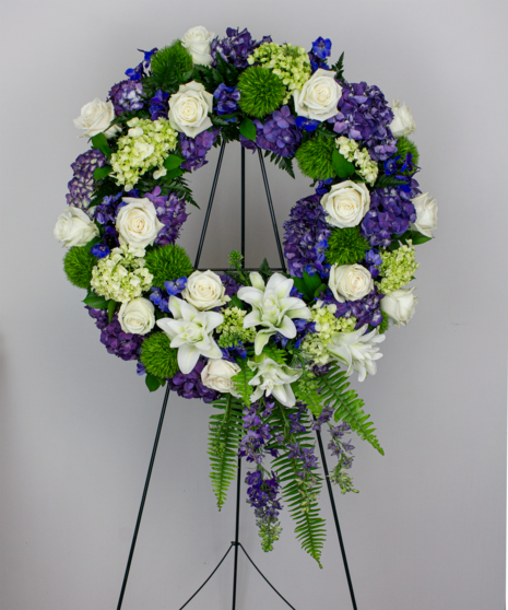 Celebrate life's truly memorable moments. This wreath features purple hydrangea, blue delphinium, green trick, white roses and lilies. 