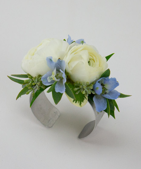 A dazzling corsage featuring two ranunculus blooms, accented with light blue delphinium.