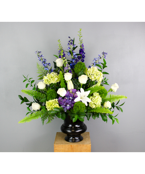 Mountain majesty urn is a stunning tribute to a loved one. This urn features purple hydrangea, white roses, white lilies, green trick, and blue delphinium. 